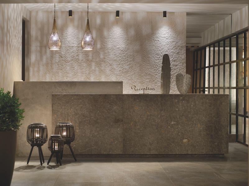 Area reception moderna dell'hotel con banco in cemento, luci eleganti e due sgabelli decorativi.