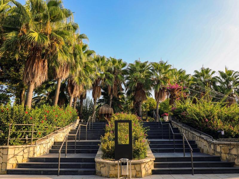 Ampia scalinata fiancheggiata da palme e cespugli verdi sotto un cielo blu limpido