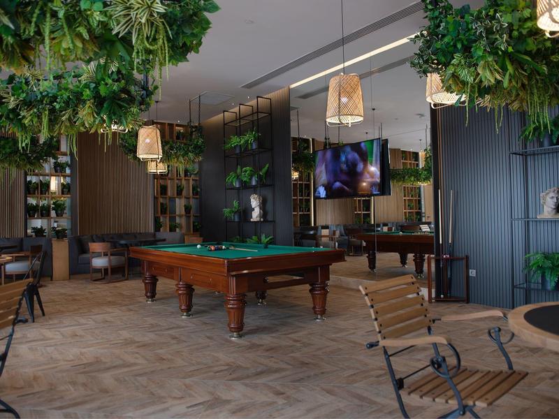 Sala giochi moderna con tavolo da biliardo, piante sospese e posti a sedere accoglienti in un hotel.
