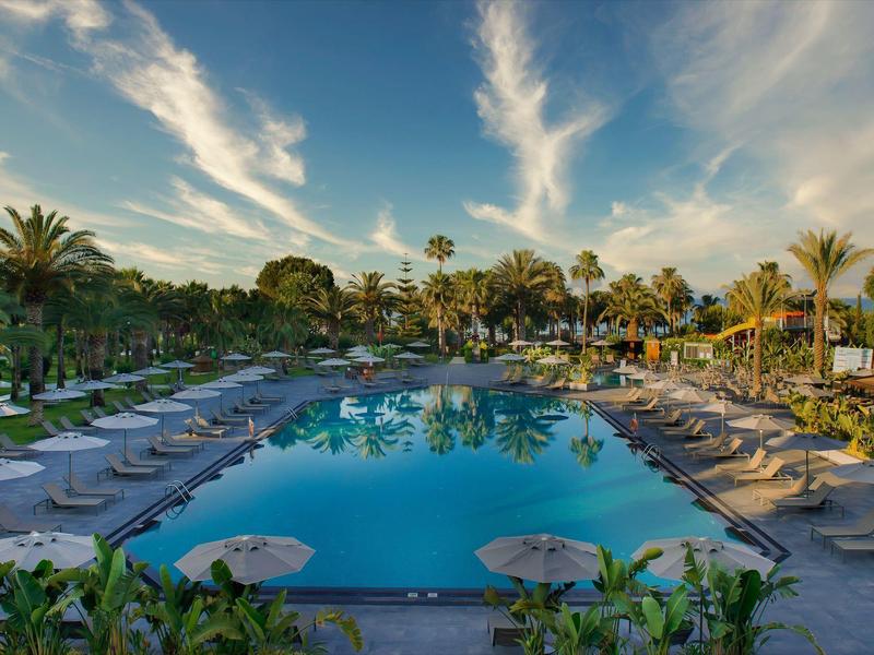 Grande piscina con lettini e palme sotto un cielo blu al tramonto.