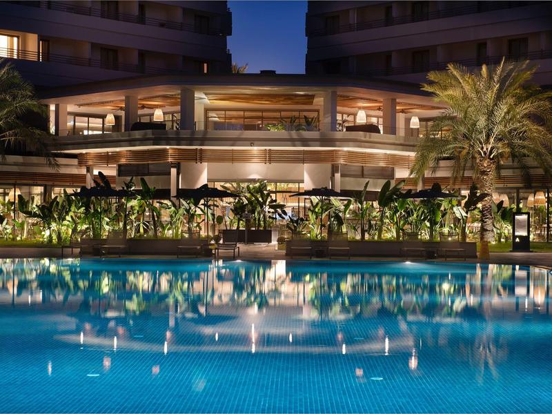 Piscina dell'hotel illuminata con piante e palme di notte.