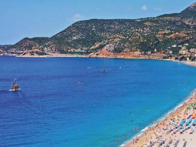 Long sandy beach with colorful umbrellas and clear blue sea near a coastal town.