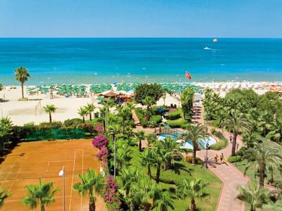 View of a beach with sun loungers, swimming pools, and tennis court in a hotel resort.