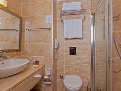 Compact hotel bathroom with sink, toilet, and glass-enclosed shower.