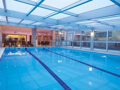 A large, bright indoor pool with blue tiles and glass roof, cozy area visible in the background.