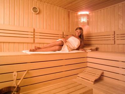 Woman relaxing in bright wooden sauna with towel and sauna bucket.