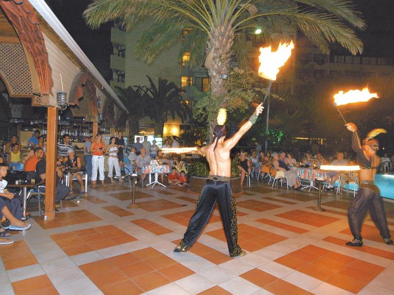 Two fire performers entertain an audience on tiled flooring at night.