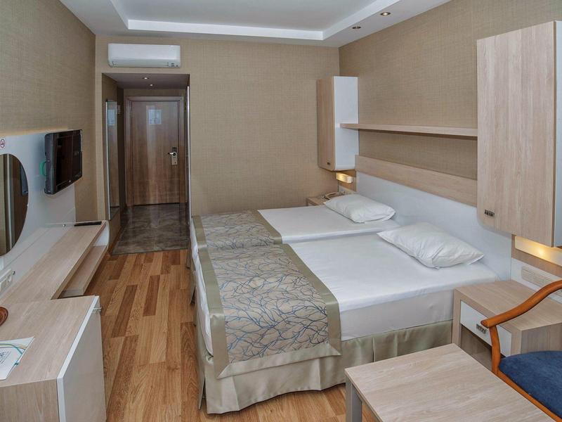 Small hotel room with double bed, desk, TV, and wooden flooring.