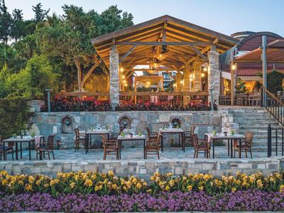 Ristorante illuminato con terrazza vicino all'acqua, circondato da piante e fiori.