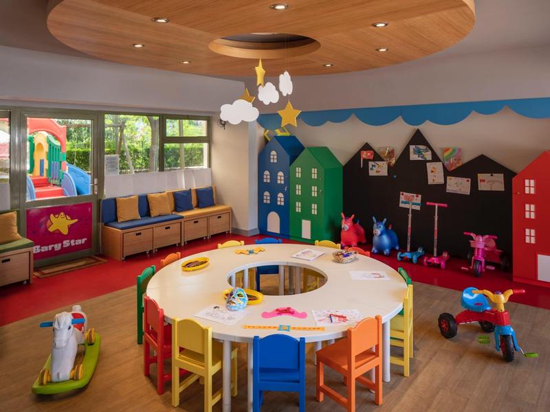 Sala giochi colorata per bambini con tavolo rotondo, sedie e giocattoli in un hotel.