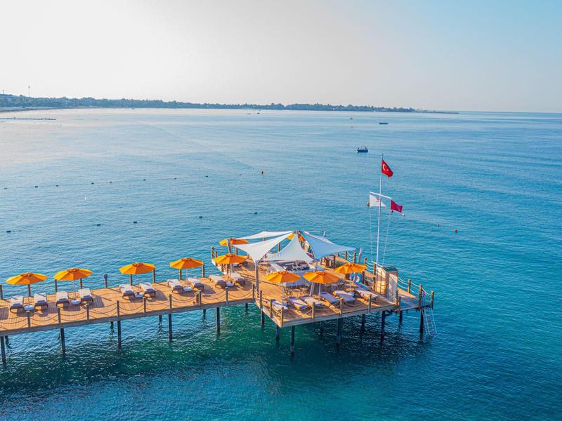 Molo in legno con ombrelloni e lettini sopra acqua blu chiara e costa distante