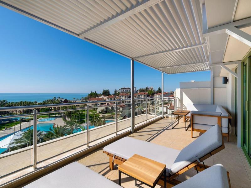 Balcone con lettini vista piscina, città e mare in una giornata soleggiata