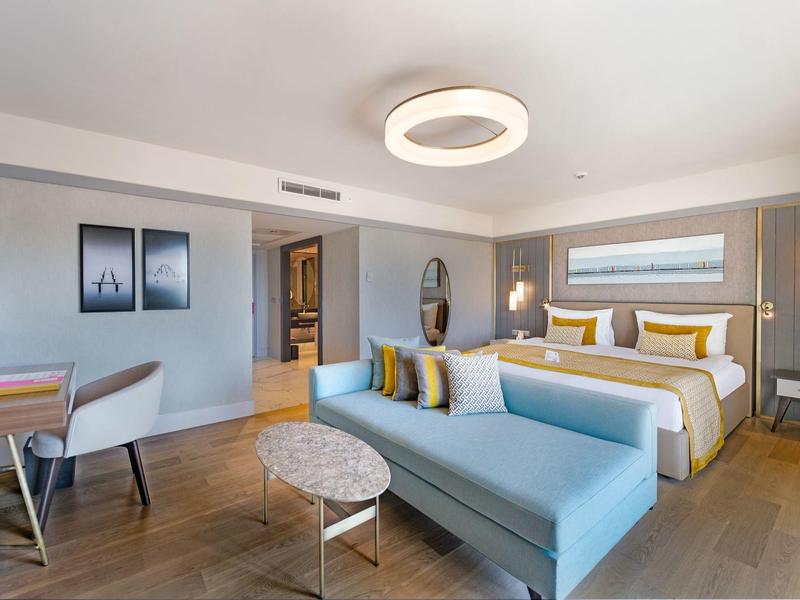 Camera d'hotel moderna con letto matrimoniale, divano, tavolo da pranzo e illuminazione elegante.