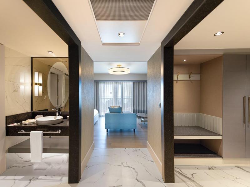 Corridoio moderno di hotel con bagno e camera da letto con copriletto blu sullo sfondo.