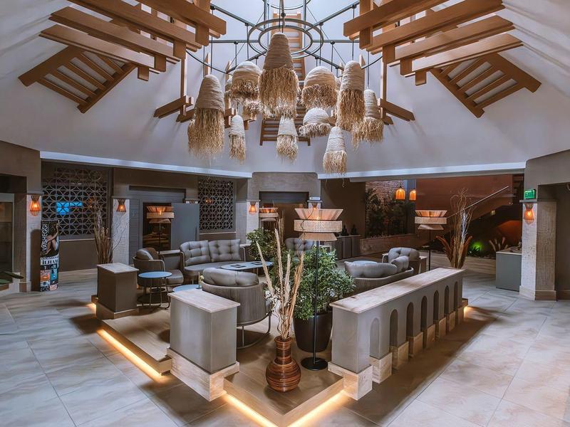 Ingresso di hotel moderno con aree salotto eleganti e lampadario decorativo in legno.