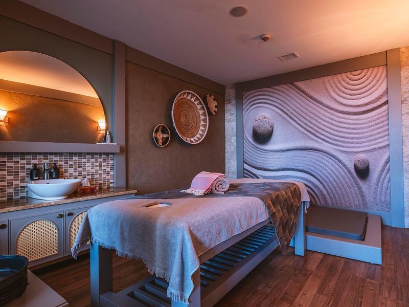 Accogliente sala benessere con lettino da massaggio, pavimento in legno e decorazioni murali rilassanti.