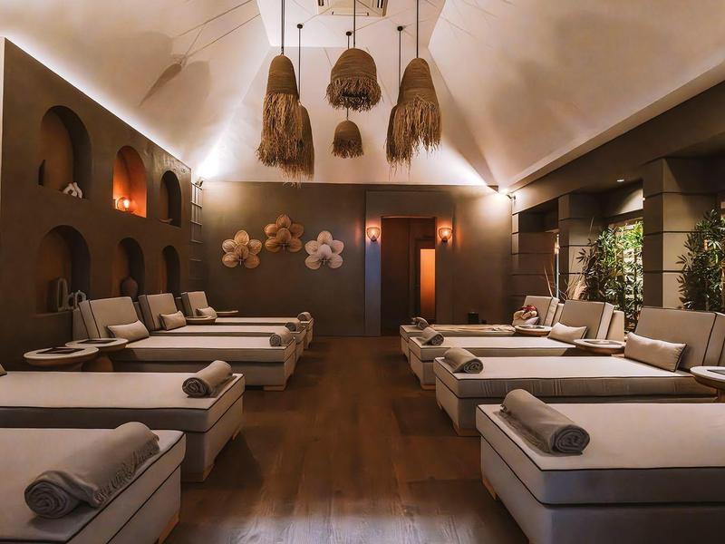 Area spa tranquilla con lettini, illuminazione soffusa e decorazioni naturali.