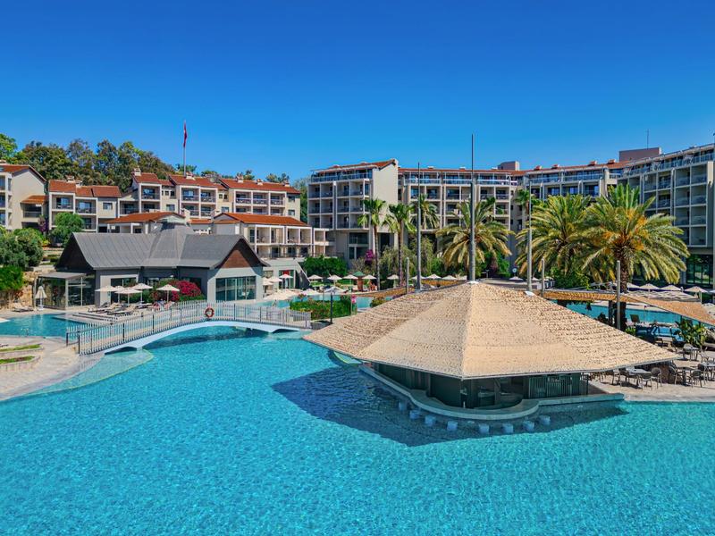 Grande piscina dell'hotel con bar swim-up, circondata da lettini e palme sotto un cielo azzurro.