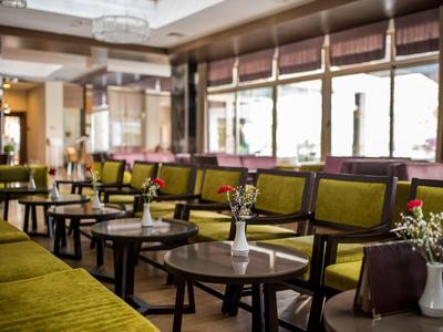 Spacious hotel lounge with olive green armchairs, wooden tables, and natural light.