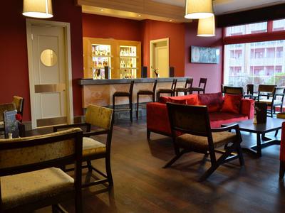 Cozy hotel lounge with red walls, dark wood furniture, and large windows letting in natural light.