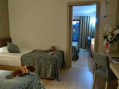 Two beds with stuffed animals, a chair, and a desk in a cozy hotel room with an open door to another room.