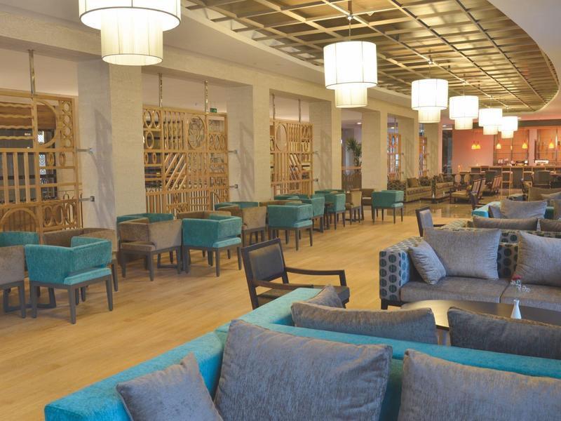 Spacious hotel lounge with cozy blue sofas, wooden floor, and warmly lit ceiling lights.