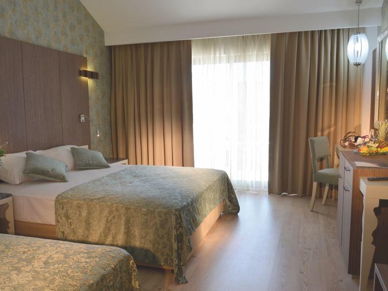 Hotel room with two beds, beige curtains, wooden floor, and a desk with a chair and lamp.
