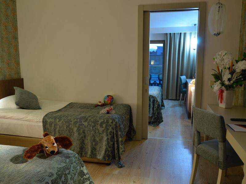 Two beds with stuffed animals, a chair, and a desk in a cozy hotel room with an open door to another room.
