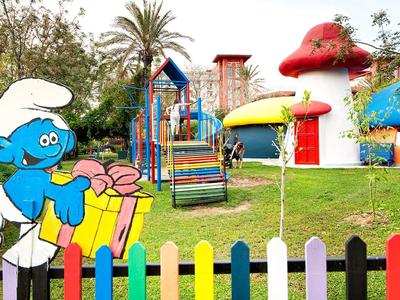 Kolorowy plac zabaw z figurką Smerfa i kolorowym ogrodzeniem.