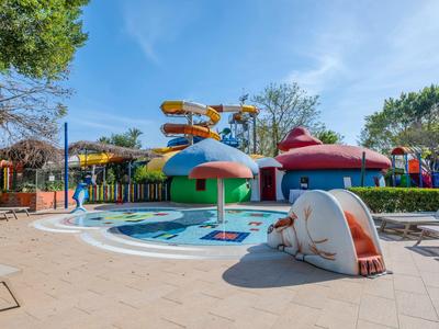 Kolorowy park wodny hotelu z zjeżdżalniami i fontanną w kształcie grzyba pod niebieskim niebem.