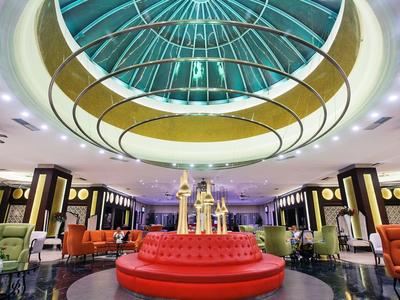 Wnętrze hotelu z okrągłym, czerwonym miejscem do siedzenia i dużą szklaną kopułą nad nim.