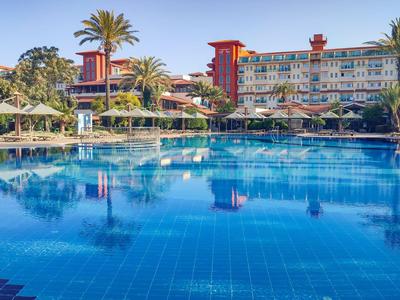 Grand piscine d'hôtel avec parasols et palmiers sous un ciel clair.