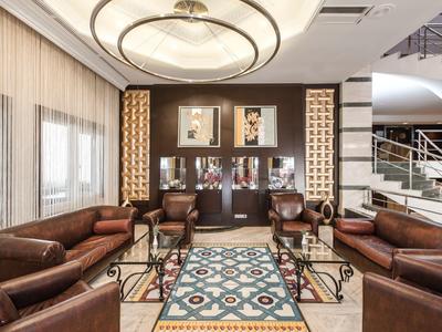 Elegancka strefa lounge hotelu z skórzanymi sofami, kolorowym dywanem i nowoczesnym oświetleniem.