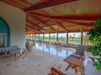 Überdachte Hotelterrasse mit gemütlichen Sitzbereichen, Holzstühlen und Blick auf Garten und Pool.