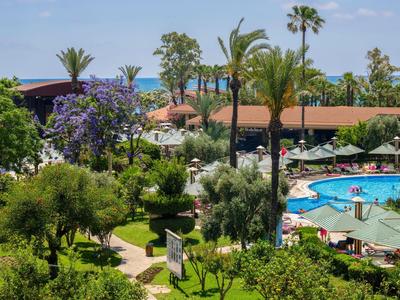 Hotelgarten mit Pool, Palmen, blühenden Bäumen und Meerblick im Hintergrund.