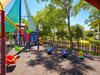 Bunter Kinderspielplatz mit Schaukeln und Rutschen neben Hotelfläche und Bäumen.