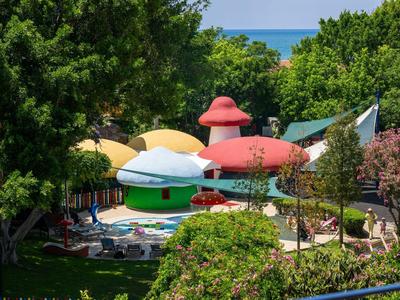 Bunte Pilzförmige Sonnenschirme und Liegestühle in einem grünen Hotelgarten bei sonnigem Wetter.