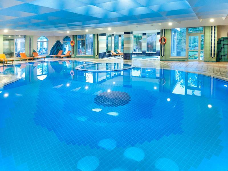 Duży, okrągły basen kryty z niebieską wodą i leżakami dookoła.