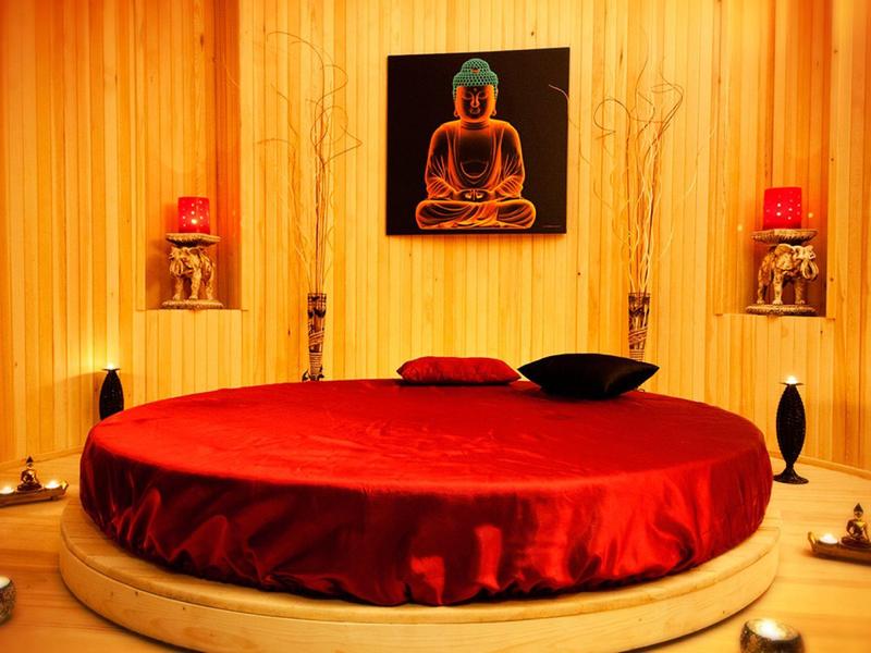 Czerwony, okrągły fotel w drewnianym, okrągłym pomieszczeniu z świecami i obrazem Buddy.