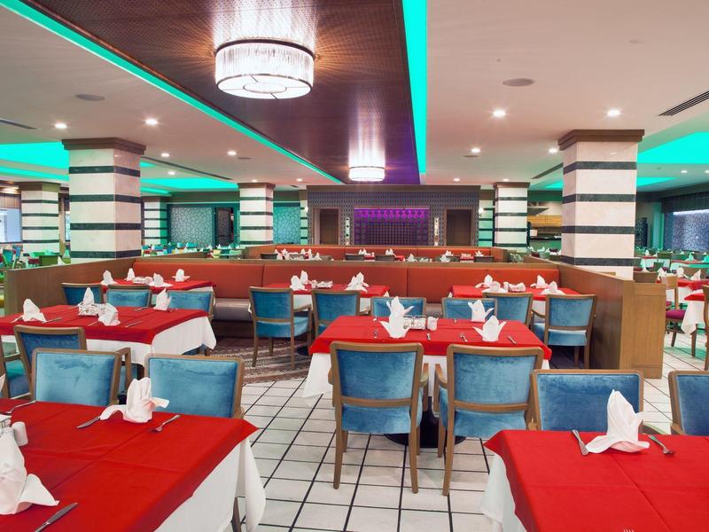 Restauracja z czerwonymi obrusami i niebieskimi krzesłami, nowoczesne oświetlenie i kolumny.