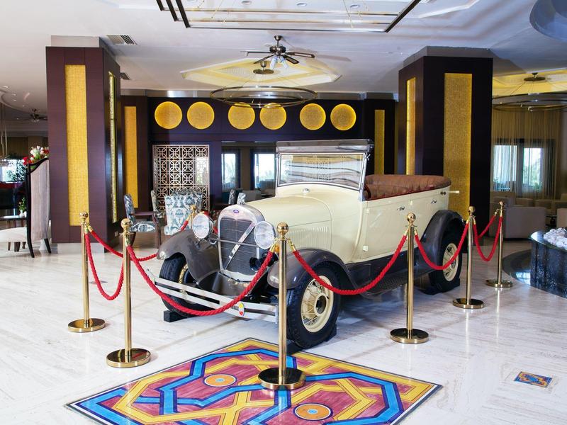 Klasyczny samochód zabytkowy w holu hotelowym za barierką w eleganckim, jasnym pomieszczeniu.