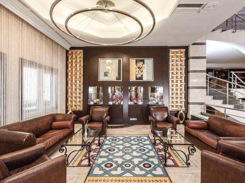 Elegancka strefa lounge hotelu z skórzanymi sofami, kolorowym dywanem i nowoczesnym oświetleniem.