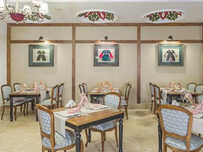 Cozy hotel dining room with wooden tables, patterned chairs, and wall art under spotlights.