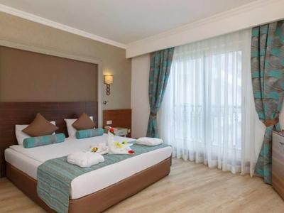 Camera d'hotel moderna con letto matrimoniale, pavimento in legno e grande finestra con tende.