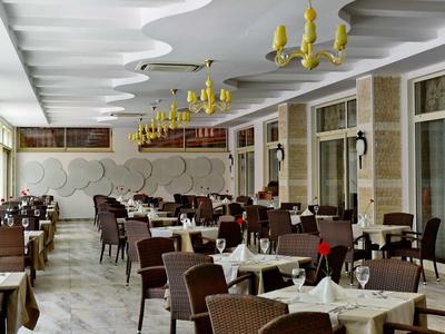 Spacious hotel restaurant with modern wicker chairs, white tablecloths, and yellow chandeliers.