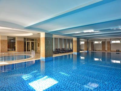 Indoor hotel pool with blue water, tiled floor, and seating area under a blue ceiling.