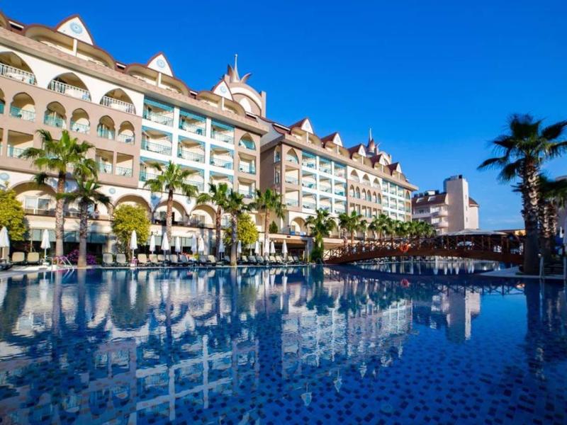 Luxury hotel with palm trees and clear blue swimming pool under sunny sky.