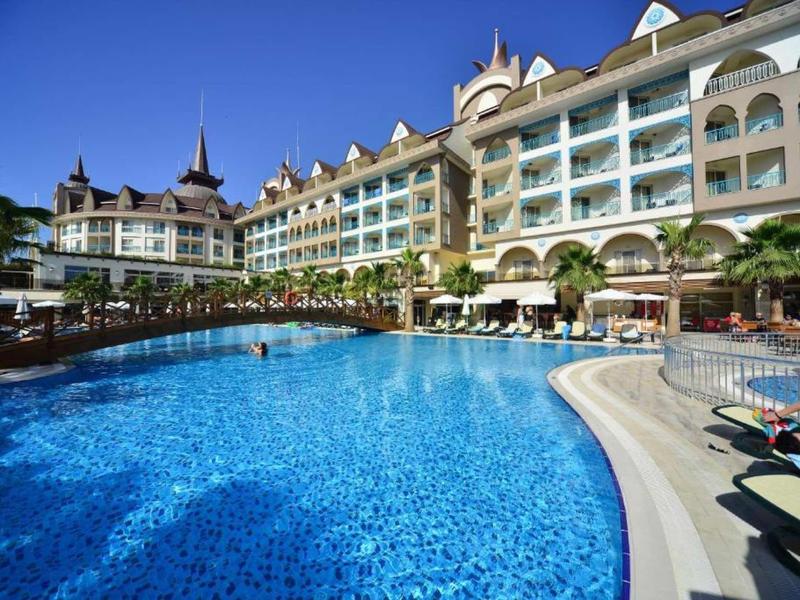 Large outdoor pool in front of a multi-story hotel with balconies and palm trees.