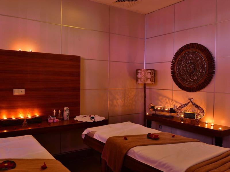 Dimly lit massage room with two beds, warm lighting, candles, and decorative wall art.