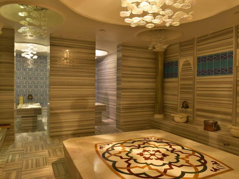 Luxurious spa room with wooden walls, intricate floor design, and soft chandelier lighting.